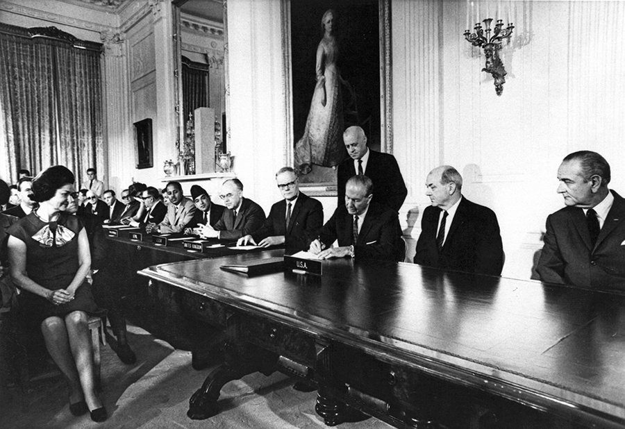 William Foster, chief U.S. negotiator on the Nuclear Nonproliferation Treaty (NPT) and director of the U.S. Arms Control and Disarmament Agency, signs the NPT July 1, 1968, as President Lyndon Johnson (far right) and Lady Bird Johnson (far left) look on. U.S. Secretary of State Dean Rusk is seated next to the president, and a number of ambassadors are seated at the far end of the table, including Soviet Ambassador Anatoly Dobrynin (fifth from right among those seated).  (Photo Courtesy of Larry Weiler)