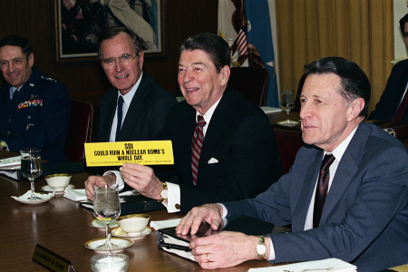 U.S. President Ronald Reagan, flanked by Vice President George H.W. Bush (L) and Defense Secretary Caspar Weinberger (R) displays bumper sticker showing support for his Strategic Defense Initiative, nicknamed Star Wars, in 1987. (Photo by Bettmann/Contributor)