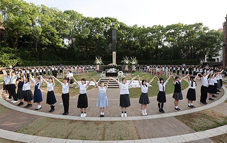 High school students, calling for a more peaceful world, form a “human chain” on Aug. 9 around the monument marking the spot where the U.S. atomic bomb fell in Nagasaki 79 years before. (Photo by STR/JIJI Press/AFP via Getty Images)