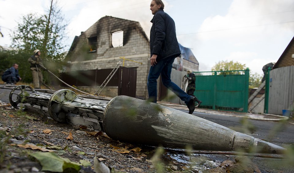 A man passes by the remains of an Uragan rocket lying in front of a burning house in Donetsk, Ukraine, on October 5. Uragan rockets can be used to deliver cluster munitions. (John Macdougall/AFP/Getty Images)